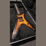 Elektrická kytara s tělem ve tvaru Flying V v barevné variantě sunburst, umístěná v černém tvrdém kufru. Nástroj má dva humbuckery, dva ovládací knof…