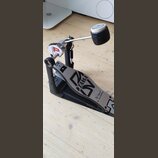 Krytý basový pedál s černým základem a stříbrným šlapadlem. Na šlapadle je viditelné logo TAMA a nápis The Legend in Innovation. Na horní části mecha…