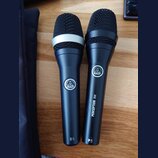 Dvě černé dynamické mikrofony značky AKG. Levý mikrofon má stříbrný prstenec pod mřížkou a nápis D5 v dolní části těla. Pravý mikrofon má nápisy PERC…