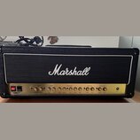 Kytarový zesilovač značky Marshall v černém texturovaném potahu s bílým lemováním mřížky. Zlatý ovládací panel obsahuje nápisy MASTER, REVERB, EQUALI…