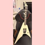Bílá elektrická kytara s ostrým, asymetrickým tvaru těla a špičatou hlavou. Na hmatníku jsou vidět obdélníkové vložky a na těle je jeden humbucker s…