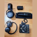 Na fotografii je sada audio vybavení: dvě černá sluchátka, mikrofon s pouzdrem a efektový pedál. První sluchátka mají nápis ZEKLER, druhá nesou logo…