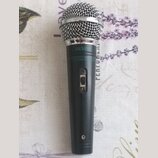 Černý dynamický mikrofon s kovovou stříbrnou mřížkou. Na horní části těla je bílý nápis DEXON a pod ním drobným písmem text ELECTRODYNAMIC MICROPHONE…