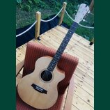 Akustická kytara s cutawayem, světlým topem a tmavým hmatníkem. Na hlavě je vidět nápis "Classic". Nástroj je umístěn na červeně vzorovaném polstrová…