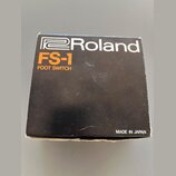 Černá kartonová krabice s bílým logem Roland. Pod ním je oranžový nápis FS-1 a bílý text FOOT SWITCH. V pravém dolním rohu je bílý nápis MADE IN JAPA…