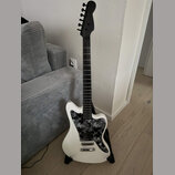 Bílá elektrická kytara s černým hmatníkem a černou hlavou. Kytara má černý pickguard s bílým květinovým vzorem a dva snímače typu single-coil. Na nás…