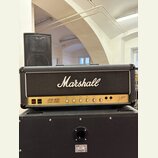 Kytarový kombozesilovač značky Marshall, model JCM 800 LEAD SERIES. Má černý kryt z textilie s bílým logem Marshall a ovládací panel s několika zlatý…