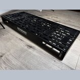 Černý kovový pedalboard s perforovaným povrchem a bočními úchopy. Na boku je bílý nápis ROCKBOARD by WARWICK a v pravém dolním rohu označení CINQUE 5…