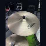 Fotografie zachycuje dva činely v mosazné barvě. Horní činel nese nápisy „Avid 6 Zildjian“ a v horní části menší text „THE GONG“. Spodní činel má náp…