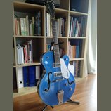 Modrá polodublová elektrická kytara s f-otvory a bílým pickguardem. Na hlavě hрифu je nápis GRETSCH a na pickguardu je viditelné logo GRETSCH. Nástro…