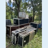 Skupina transportních case různých velikostí a barev (černé, hnědé, stříbrné) umístěná na trávníku. Na jedné z černých case je viditelný nápis ACCUSR…
