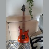 Elektrická kytara s oranžovým lakovaným tělem a hnědým hnedým hmatníkem. Na hlavě je vidět bílý nápis "Ibanez". Kytara má dva humbuckery, jeden ovlád…