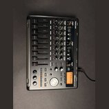 Černý digitální multitrackový nahrávací studiový mixér značky TASCAM, model DP-02. Zařízení obsahuje několik faderů, otočných knoflíků a ovládacích t…