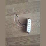 Bílý snímač typu single-coil s pěti viditelnými magnetickými póly. K snímači vedou dva volné vodiče, jeden bílý a jeden černý. Snímač je upevněn dvěm…