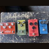 Čtyři efektové pedály v řadě. Horní oranžový pedál nese nápisy „mod“, „MODULAR LUNAR / PHASER“ a logo „M-audio“. Druhý pedál je zelený s žlutým ornam…