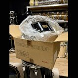 V kartonové krabici s nápisem SNARE DRUM a logem TAMA je umístěn černý malý buben zabalený v průhledné plastové fólii. Na korpusu nástroje je viditel…