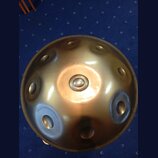 Kovový perkusní nástroj typu steel tongue drum v bronzové barvě. Nástroj má kulovitý tvar s několika vlisnými otvory rozmístěnými po povrchu. Povrch…