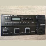 Černý kytarový procesor s nápisem BOSS GT-1 GUITAR EFFECTS PROCESSOR. Zařízení obsahuje displej, tři ovládací knoflíky, řadu tlačítek a dvastředý ped…