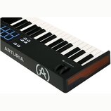 Černý MIDI kontrolér s klávesnicí a modrými podsvícenými pady. Na boku je bílý nápis ARTURIA a logo ve tvaru stylizedovaného písmene A v kruhu. V pra…