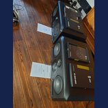 Dva černé studiové monitory značky ADAM AUDIO řady S SERIES. K reproduktorům jsou přiloženy krabice s nápisem ADAM AUDIO S SERIES a dva papírové cert…
