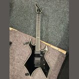 Černá elektrická kytara s ostře hranatým korpusem a bílým lemováním. Na hlavě hmatníku je viditelné logo "Jackson". Nástroj má dva humbuckery, černý…