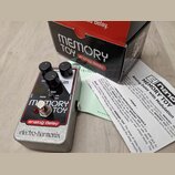 Kytarový efekt v kovovém šedém šasi s červeným ovládacím panelem. Na panelu jsou tři černé otočné knoflíky s popisky DELAY, MOD a FEED BACK, přepínač…