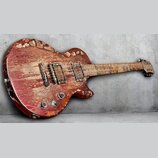 Červená elektrická kytara s trupem ve tvaru Les Paul. Nástroj vykazuje extrémní opotřebení, lak je na mnoha místech odloupaný a povrch je silně poškr…