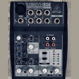 Tmavě šedý mixážní pult s bílými a červenými popisky. Na horní části je nápis XENYX 502, pod ním text PREMIUM 5-INPUT 2-BUS MIXER • XENYX MIC PREAMP…