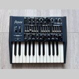 Černý analogový syntetizátor s klaviaturou, na kterém je vlevo nápis Arturia MUSICAL INSTRUMENTS a vpravo MINIBRUTE ANALOG SYNTHESIZER. Přístroj obsa…