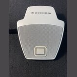 Bílý mikrofon s kovovou mřížkou a logem SENNHEISER v horní části. V dolní části mřížky je umístěno čtvercové tlačítko. Povrch plastového těla vykazuj…
