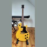 Žlutá elektrická kytara typu Les Paul s černým pickguardem a černými knoflíky. Na hlavě hmatníku je bílý nápis "Tokai". Nástroj je umístěn na černém…