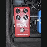 Červený kytarový efekt s nápisy HALL OF FAME REVERB a tc electronic. Na horní straně jsou čtyři černé ovládací knoflíky s popisky DECAY, PRE-DELAY, T…