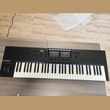 Černý MIDI kontrolér s klávesnicí. Na levé straně je bílý nápis KOMPLETE s logem vedle. Horní panel obsahuje několik sad tlačítek, dva displeje a jed…