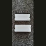 Dvě bílé obdélníkové snímače s montážními otvory po stranách. Horní snímač má v pravém dolním rohu nápis EMG. Dolní snímač má v pravém dolním rohu ná…