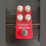 Červený kytarový efekt s bílými oválnými knoflíky. Na zařízení jsou nápisy OUTPUT, SUSTAIN, TONE a ATTACK, dále text COMPRINCE VINTAGE COMPRESSOR a z…