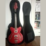 Červená polodublová elektrická basová kytara v černém tvrdém pouzdře. Na hlavě nástroje je bílý nápis Studio Bass. Kytara má dva snímače, dva ovládac…
