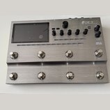 Stříbrný efektový procesor s kovovým povrchem a displejem. Na horním panelu je nápis GE3CC Amp modeling & Multi effects, dále označení EXP1, EXP2, XL…