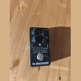 Černý kytarový efekt s nápisy DARK MATTER DISTORTION a tc electronic. Na horní straně jsou čtyři otočné oválné knoflíky s popisky LEVEL, VOICE a TREB…