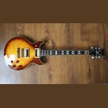 Elektrická kytara s tvarem singlecut a povrchovou úpravou sunburst v žlutých a hnědých tónech. Na hlavě je viditelné logo s nápisem Ibanez. Nástroj m…