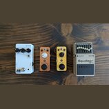 Čtyři kytarové efekty v řadě na dřevěném povrchu. Zleva: bílý pedál s nápisy REVERB, JHS 3 SERIES a ovládacími prvky VERB, EQ, DECAY a PRE DELAY. Dru…