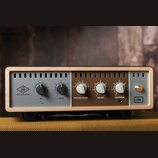 Audio zařízení v dřevěném rámu s šedým a hnědým předním panelem. Na levé straně je logo UA a nápis UNIVERSAL AUDIO, vedle něj knoflíky s popisky RIG…