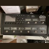 Černý kytarový procesor s displejem a ovládacími tlačítky. Na pravé straně je bílý nápis FRACTAL AUDIO SYSTEMS a model FM9 AMP MODELLER / FX PROCESSO…