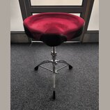 Fotografie zobrazuje bubenícký stolec s trojnožkou z chromovaného kovu. Sedací část je potažená červeným a černým materiálem, který vykazuje mírné po…