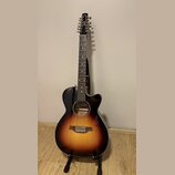 Akustická kytara s 12 strunami v černé barvě s přechodem do oranžové a žluté (sunburst). Na hlavě hmatníku je bílé logo s nápisem "Cort". Nástroj je…