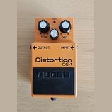 Kytarový efekt v oranžovém provedení s černým spínacím pedálem. Na šasi jsou nápisy Distortion, DS-1 a na pedálu logo BOSS. Horní část obsahuje tři o…