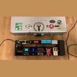 Stříbrný hliníkový kufr s různými nálepkami, včetně nápisů SPACESHIP, TONERIDER a KingTone. Pod kufrem je černý pedalboard s napájecím trafem Caline…