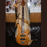 Elektrická basová kytara s přírodním dřevěným povrchem a hnědým hmatníkem. Nástroj má dva černý humbuckery, čtyři ovládací knoflíky a černý popruh. N…