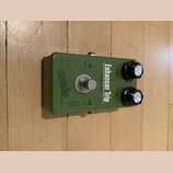 Zelený efekt pedál s kovovým šasi a dvěma černými ovládacími knoflíky s kovovými vršky. Na horní straně je nápis Enhancer Trip a Sonic Filter, vlevo…