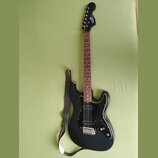 Černá elektrická kytara s černým pickguardem a hnedým hmatníkem. Na hlavě je bílý nápis SPIRIT. Kytara má tři snímače typu single-coil a je k ní přil…