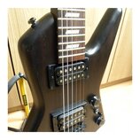 Černá elektrická kytara s tmavým hmatníkem a bílými vložkami. Nástroj má dva černý humbuckery a dva ovládací knofíky. Kytara je umístěna v žlutém sto…
